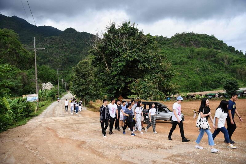 Visitors walking down the road away from the Tham Luang cave, where 12 boys from the "Wild Boars" football team and their coach were trapped last year, in the Mae Sai district of Chiang Rai province. AFP