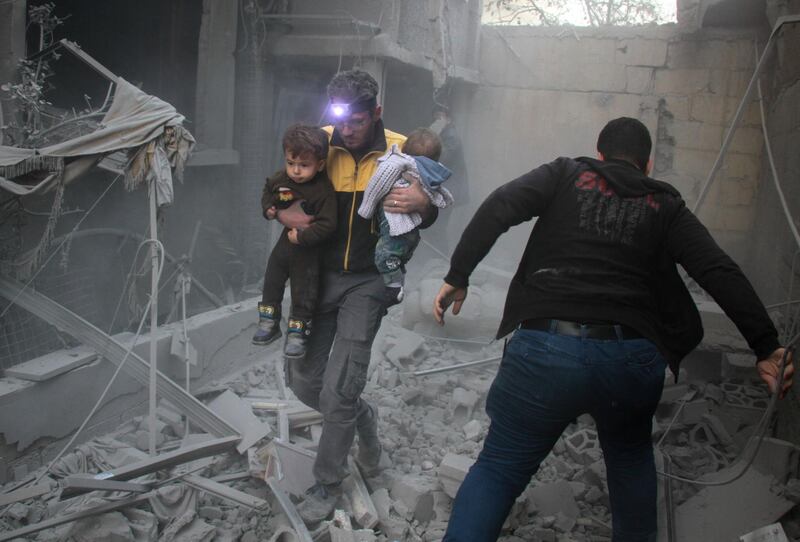 A Syrian man carries two children from the rubble of buildings destroyed by Syrian government air strikes in Douma on February 7, 2018. Hamza Al Ajweh / AFP