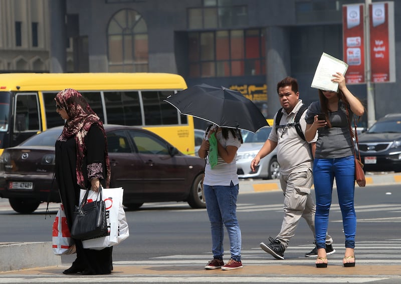 Pedestrians use an umbrella and paper to create shade for their faces and heads in the searing Abu Dhabi heat. Ravindranath K / The National
