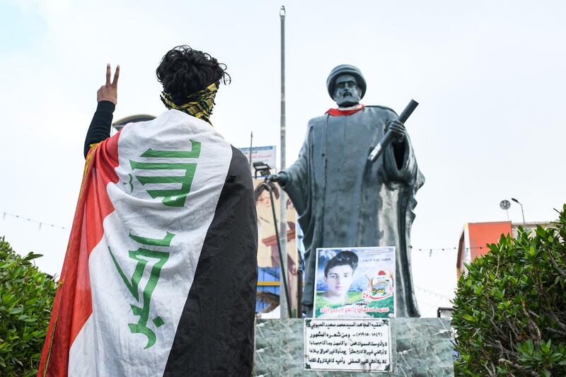 A youth draped in an Iraqi national flag gestures while standing before a statue of 19th century Iraqi cleric and poet, Mohamed Said al-Habboubi (1849-1915). Anti-government demonstrators are gathering at the square named after the cleric, in Iraq's southern city of Nasiriyah in Dhi Qar province. AFP