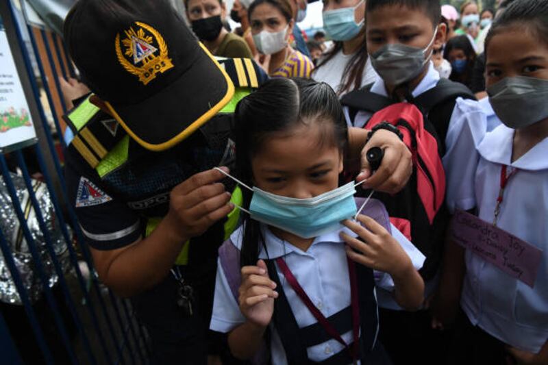 A city hall employee helps a pupil put on a face mask in Quezon city. AFP