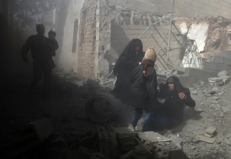 A Syrian woman is helped to her feet during regime air strikes in Jisreen on February 8, 2018. Abdulmonam Eassa / AFP