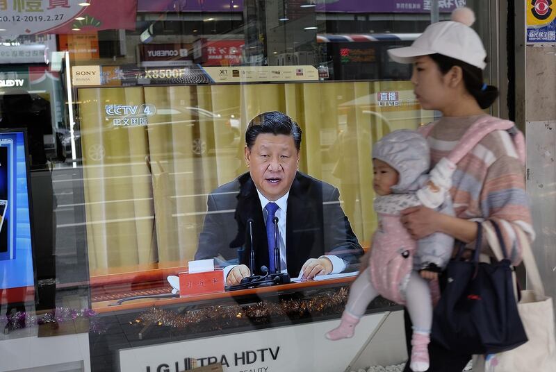 A mother carries her child past a television in New Taipei City on January 2, 2019 showing China's leader Xi Jinping making a speech commemorating the 40th anniversary of a message sent to Taiwan in 1979. Taiwan's unification with the mainland is "inevitable", President Xi Jinping said on January 2, warning against any efforts to promote the island's independence and saying China would not renounce the option of using military force to bring it into the fold. / AFP / Sam YEH
