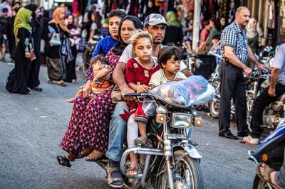 A man rides a motorcycle with a woman and children through a street market in the predominantly-Kurdish northeastern Syrian city of Qamishli on August 5, 2019. - On August 4, Turkey's President Recep Tayyip Erdogan said his country was running out of patience with floundering US efforts to set up a buffer zone along its southern border in northeastern Syria. The Kurdish People's Protection Units (YPG) have been a key US ally in the fight against the Islamic State jihadist group in the region where the Kurds maintain an autonomous administration. (Photo by Delil SOULEIMAN / AFP)