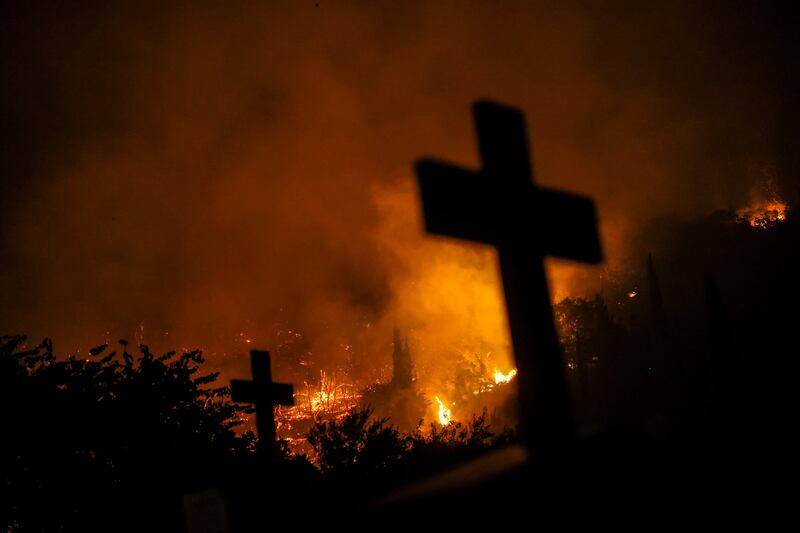 Crosses from graves are silhouetted as a wildfire burns in the village of Latas, Greece. Reuters 