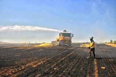 Syrian Civil Defence volunteers try to extinguish a fire in a field of crops in Kfar Ain, Idlib. AP  