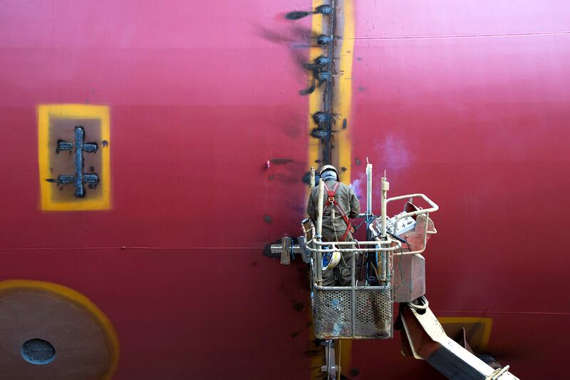 An employee works on an elevated work platform next to a ship under construction.