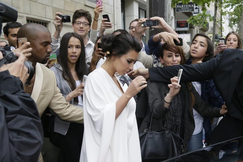 People gather around Kim Kardashian, centre, and Kanye West, left, as they leave their residence in Paris on May 23, 2014, before their wedding. AFP