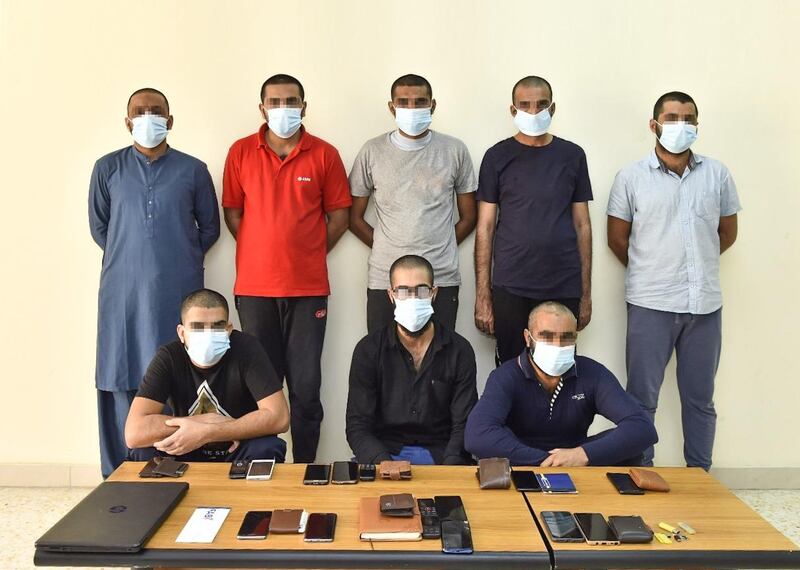 Eight of the men, along with laptops and phones seized by police. Courtesy Sharjah Police