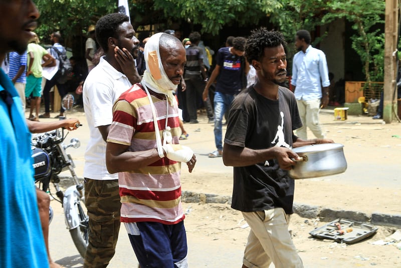 A wounded Sudanese demonstrator follows a protester carrying a pot of food. AFP
