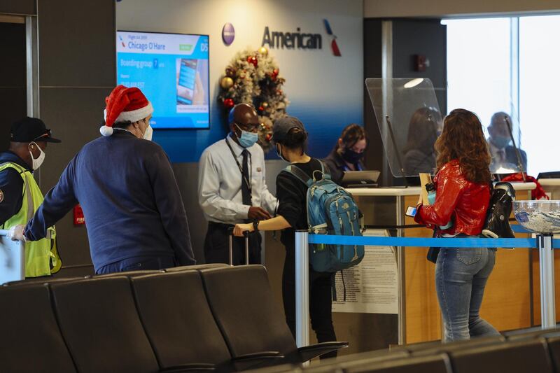 A worker wears a Santa hat as travelers wearing protective masks board an American Airlines Group Inc. flight at LaGuardia Airport (LGA) in New York, U.S., on Thursday, Dec. 24, 2020.  New York Mayor Bill de Blasio said the city will strictly enforce quarantine rules for all travelers arriving in the city during the holidays, particularly those from the U.K., where a highly contagious new Covid-19 strain has been detected. Photographer: Angus Mordant/Bloomberg