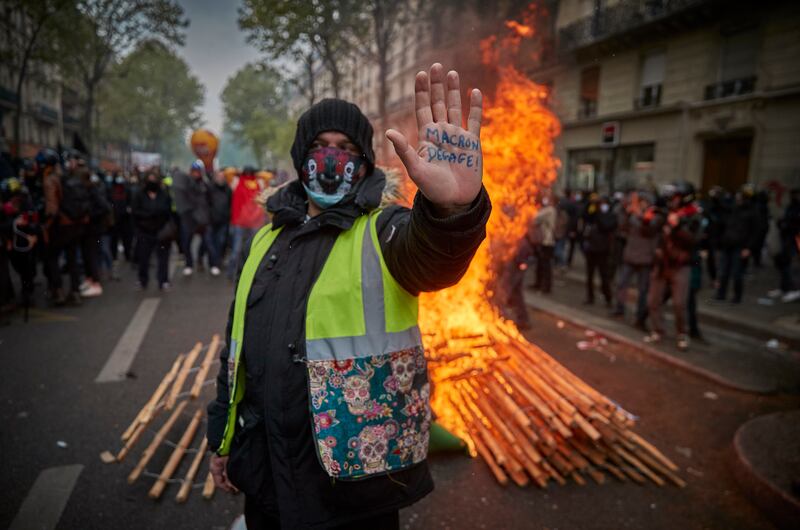 A yellow vest protester stands in front of a burning barricade as May Day protests turn violent near Place de la Republique in May 2021.