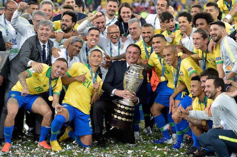 (FILES) In this file photo taken on July 07, 2019, Brazilian President Jair Bolsonaro holds the Copa America trophy as members of the Brazilian national team celebrates after winning the title by defeating Peru in the final match of the football tournament at Maracana Stadium in Rio de Janeiro, Brazil. With two weeks to kickoff, South America's CONMEBOL football federation on May 31, 2021 moved the Copa America 2021 to Brazil after stripping Argentina of matches amid a Covid-19 surge, and co-host Colombia due to social unrest. / AFP / Carl DE SOUZA
