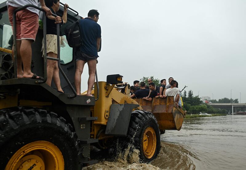 People hitch a ride on a wheel loader to cross a flooded street in Zhengzhou.