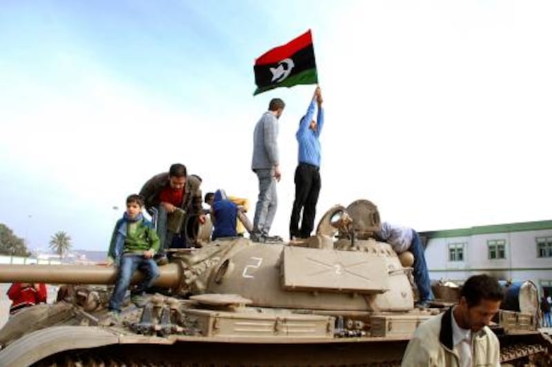 Residents stand on a tank holding a pre-Gadhafi era national flag inside a security forces compound in Benghazi, Libya on Monday, Feb. 21, 2011. Libyan protesters celebrated in the streets of Benghazi on Monday, claiming control of the country's second largest city after bloody fighting, and anti-government unrest spread to the capital with clashes in Tripoli's main square for the first time. (AP Photo/Alaguri) *** Local Caption ***  CAI125_APTOPIX_Libya_Protests.jpg