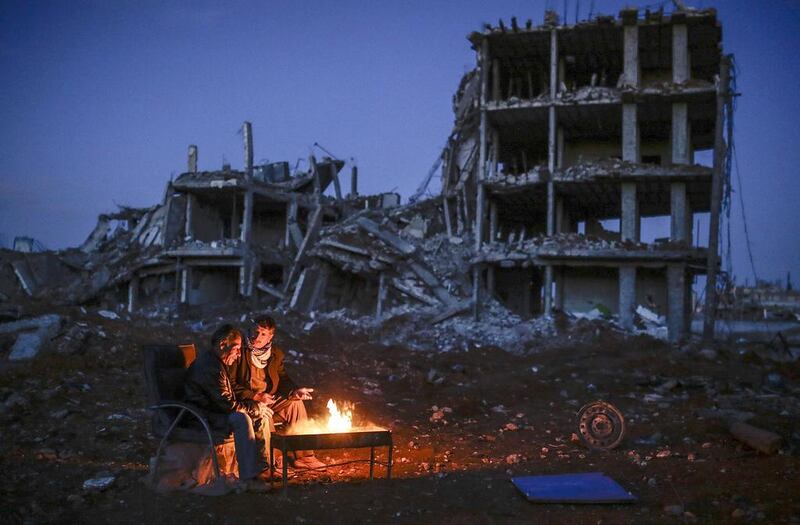 Kurds sit near a destroyed building in Kobani, on the Turkish border, this week. After earning praise from the White House for retaking the town, with support from US-led airstrikes, Syria’s Kurdish fighters say they have been forgotten.  Yasin Akgul / AFP

