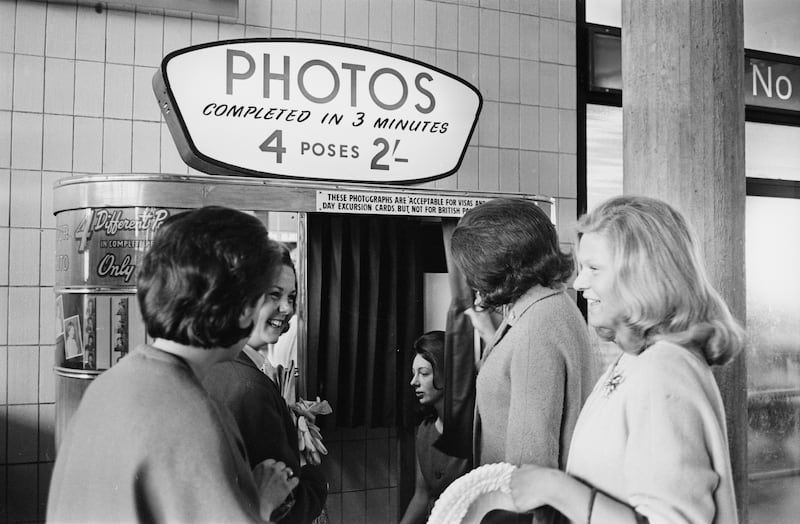 A group of young women wait to use a photo booth machine to obtain passport style photos at Gatwick Airport in 1963