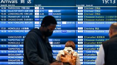 People stand in front of an arrivals board showing cancelled flights at Tokyo's Haneda international airport. AFP