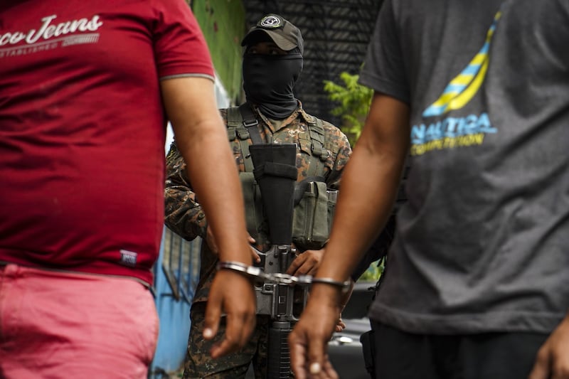 A member of the military stands guard behind two alleged gang members in San Salvador. Bloomberg