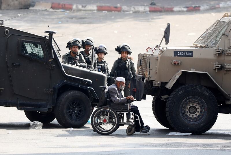 An elderly Palestinian man in wheelchair passes in front of Israeli soldiers at the site of clashes with protesters in the occupied West Bank city of Hebron. EPA