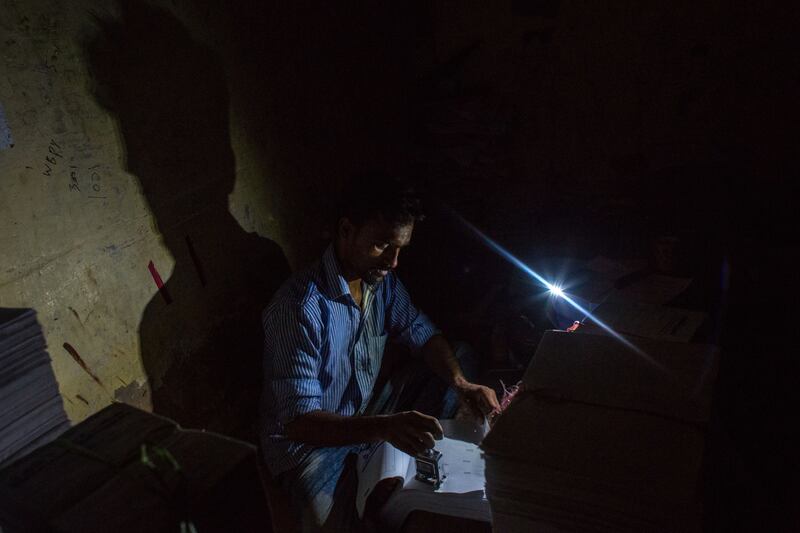 A man uses his mobile phone torch to work at a printing press during a load-shedding power outage.