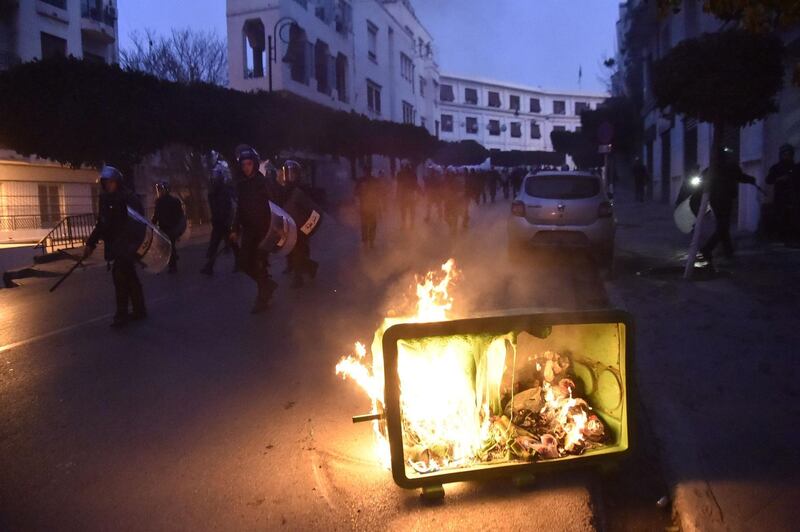 Members of the Algerian security forces patrolling a street in the capital Algiers, walk past a garbage container set ablaze by protesters during a demonstration. AFP