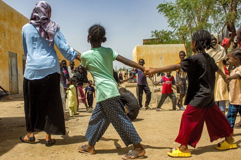A woman walks with children in a circle during an activity at a refugee camp in Al Suwar
