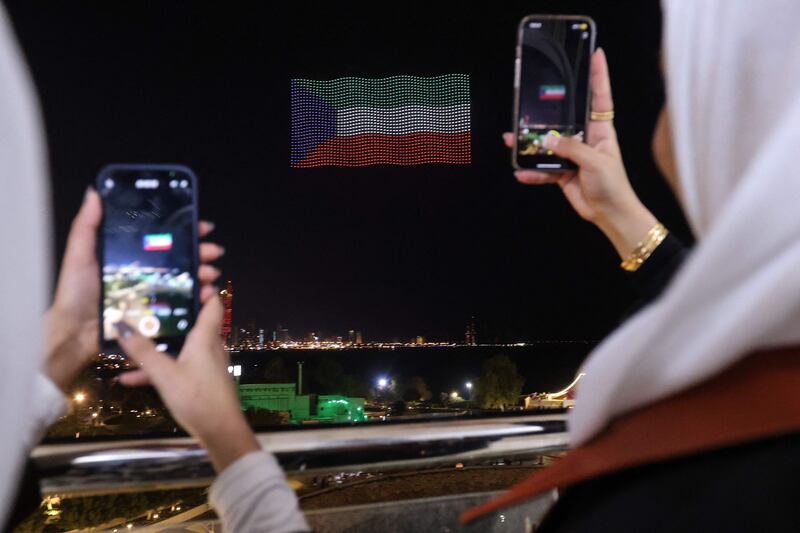 Women photograph an image of Kuwait's national flag made of drones above Green Island off the coast of Kuwait City 
