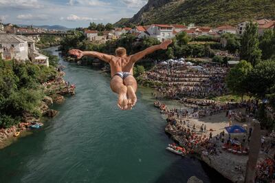 MOSTAR, BOSNIA AND HERZEGOVINA - JULY 26: A competitor dives from Start Most (Old Bridge), the Ottoman era bridge destroyed in the country's 1992-95 war and later restored, during the 454th traditional diving competition on July 26, 2020 in Mostar, Bosnia and Herzegovina. The internationally mediated power-sharing deal has been approved by parliament and an election date has been set for December 20th. The Bosniak minority want to ensure they are not out-voted and the Croat majority are pushing for the town's unification.  (Photo by Damir Sagolj/Getty Images)