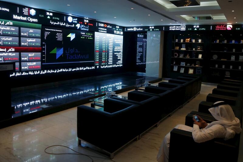 FILE PHOTO: A trader uses his mobile as he monitors screens displaying stock information at the Saudi Stock Exchange (Tadawul) in Riyadh June 15, 2015. REUTERS/Faisal Al Nasser/File Photo