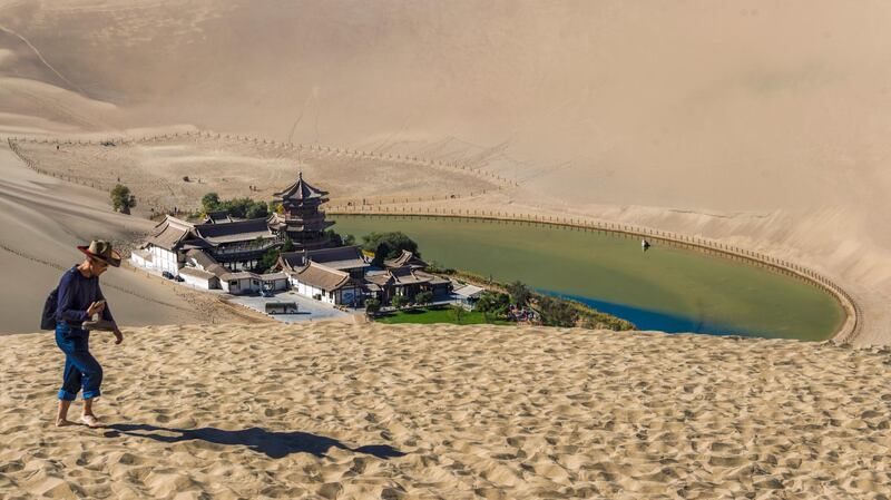 A man climbs dunes near Crescent Lake in Dunhuang.