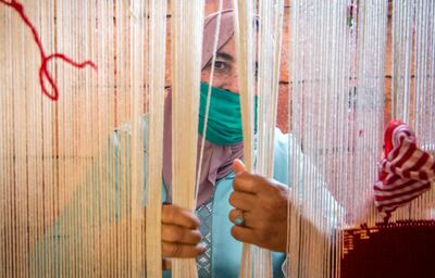 A Moroccan rug weaver peeks from behind carpet thread at a workshop in the city of Sale, north of the capital Rabat, on June 3, 2020, during the novel coronavirus pandemic.  Artisans in Morocco have been starved of income for almost three months because of the COVID-19 pandemic. The crafts industry represents some seven percent of GDP, with an export turnover last year of nearly 1 billion dirhams ($100 million). / AFP / FADEL SENNA

