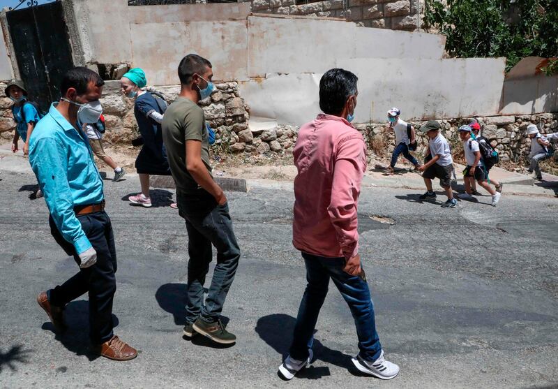 Palestinian men walk past a group of Israeli settlers as they walk home on al-Shuhada street in the H2 area of the city of Hebron, in the occupied West Bank.  AFP