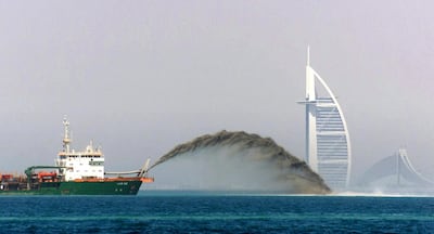 A dredger barge pumps sand onto the sea bed 3 miles off the shore of Dubai as the Palm Island development gets in full gear 05 May 2002, with the Burj al-Arab and Jumairah beach hotels in the background. The ambitious project comprises the creation of an palm tree-shaped artificial island on which there will be hotels, beaches, marinas and residential buildings.     AFP PHOTO/Jorge FERRARI (Photo by JORGE FERRARI / AFP)