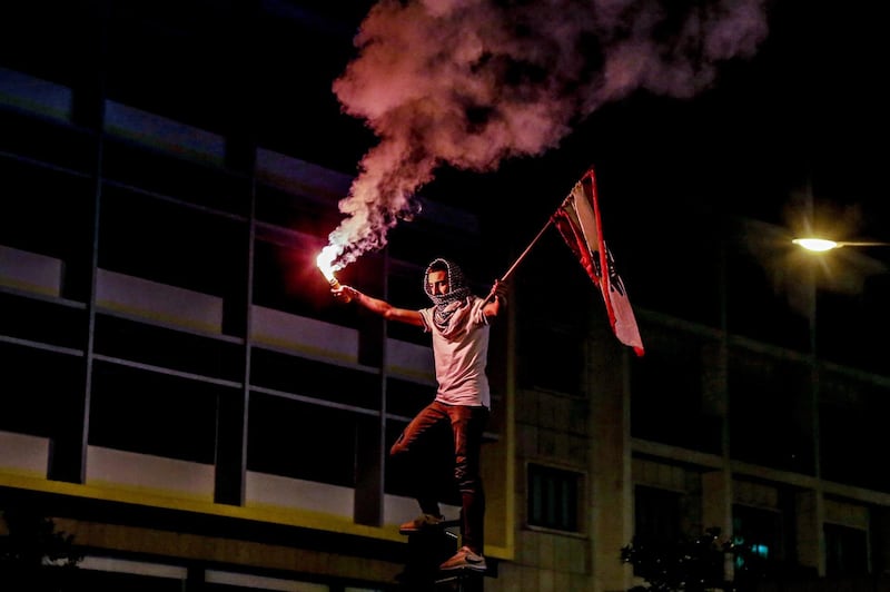 A protester lights a flare and waves Lebanese flag during ongoing anti-government protests in front the government palace in downtown Beirut, Lebanon.  EPA