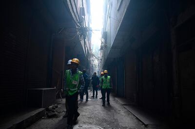 Workers from BSES Yamuna Power Limited walk on a street near a factory site where a fire broke out a day before, in Anaj Mandi area of New Delhi on December 9, 2019. At least 43 people were killed on December 9 in a devastating fire that ripped through a bag factory in the congested old quarter of the Indian capital New Delhi, with survivors describing the screams of workers trapped inside. / AFP / Sajjad  HUSSAIN

