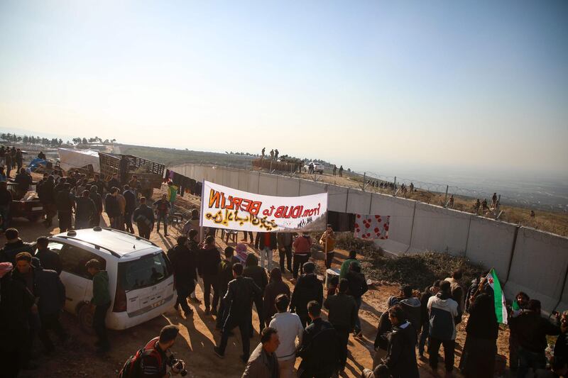 Syrians gather during a symbolic protests in the city of Harim in the rebel-held northern countryside of Syria's Idlib on the border with Turkey on January 2, 2020. Hundreds of Syrian men, women and children marched towards the frontier demanding to be allowed through in a symbolic protest, an AFP correspondent said. Near the Syrian border town of Harem, women lugged bags and men carried small children towards the razor-wired wall blocking the way to Turkey, he said. "From Idlib to Berlin," read one banner, referring to the German capital many Syrians dream of reaching as they escape the war. / AFP / AAREF WATAD
