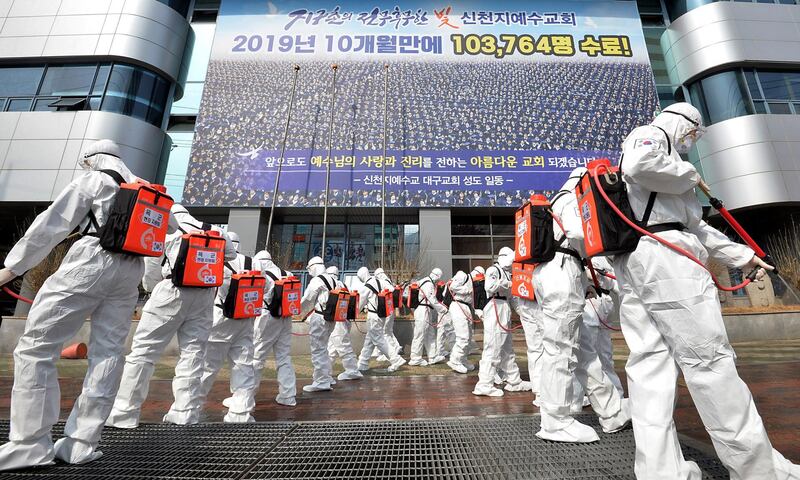 Army soldiers wearing protective suits spray disinfectant to prevent the spread of the coronavirus in front of a branch of the Shincheonji Church of Jesus in Daegu, South Korea, Sunday, March 1, 2020. The coronavirus number of cases shot up in Iran, Italy and South Korea and the spreading outbreak shook the global economy. (Lee Moo-ryul/Newsis via AP)