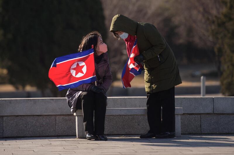 In a photo taken on December 24, 2020 two women hold North Korean flags as they sit in a park in front of the Grand People's Study House in Pyongyang. (Photo by KIM Won Jin / AFP)