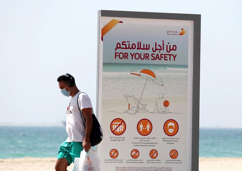 Dubai, United Arab Emirates - Reporter: N/A. News. Covid-19/Coronavirus. A man walks passed a safety sign on the beach with his shopping. Sunday, June 21st, 2020. Jumeriah, Dubai. Chris Whiteoak / The National