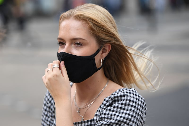 A shopper adjusts her face covering as she walks along Oxford Street in central London.