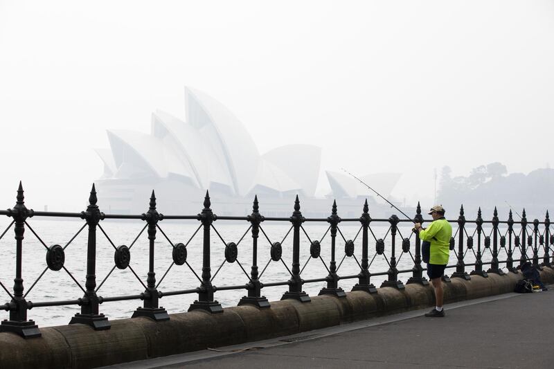 An angler fishes as the Sydney Opera House stands shrouded in haze in Sydney, New South Wales, Australia. Bloomberg