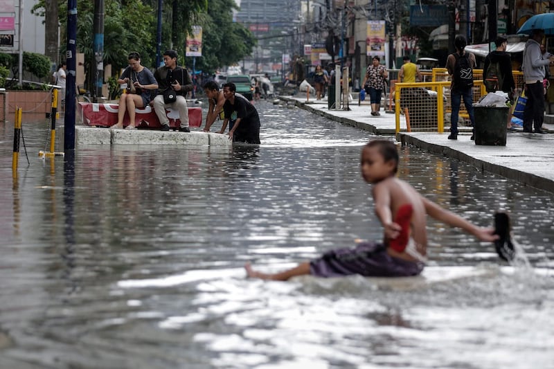 A boy plays as people ride on a raft to cross a flooded road in Makati, south of Manila, Philippines. EPA