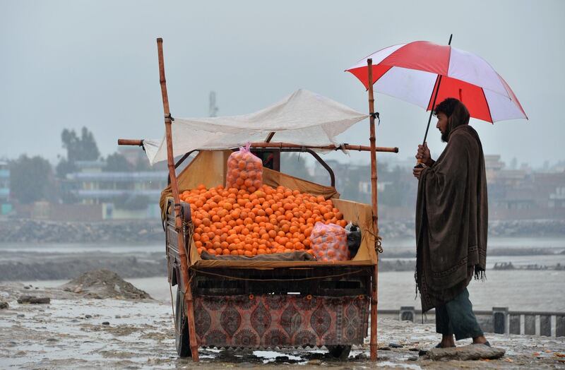 An Afghan street vendor selling oranges waits for customers on a rainy day on the roadside in Jalalabad. AFP