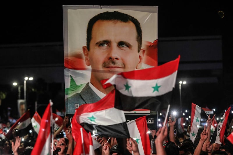 TOPSHOT - Syrians wave national flags and carry a large portrait of their president as they celebrate in the streets of the capital Damascus, a day after an election set to give the current President Bashar al-Assad a fourth term, on May 27, 2021. The election held yesterday in government-held areas was the second presidential vote in Syria since the start in 2011 of a war that has left over 388,000 dead.  / AFP / LOUAI BESHARA
