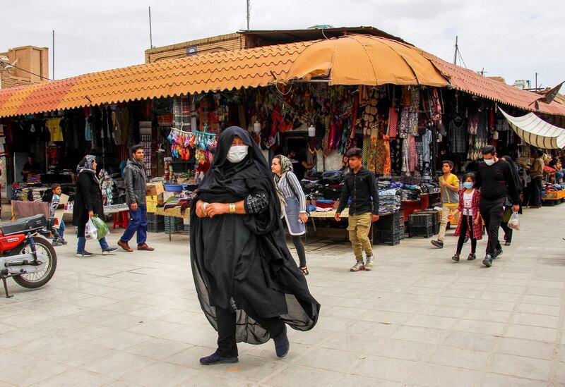 Iranians, some wearing personal protective equipment, walk past shops in the southeastern city of Kerman, Iran. AFP