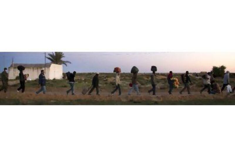 West African migrants walk towards their tents at a UN camp near Ras Ajdir. Refugees are eating meals donated by local restaurants with many sleeping in schools and youth hostels.