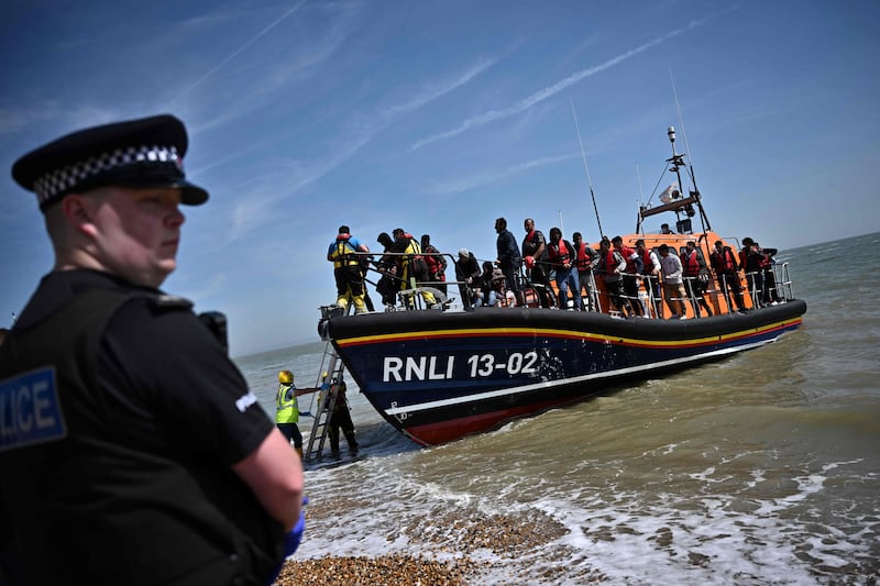 A police officer stands guard on the beach at Dungeness, England, as migrants get off a lifeboat after they were picked up at sea in June. AFP