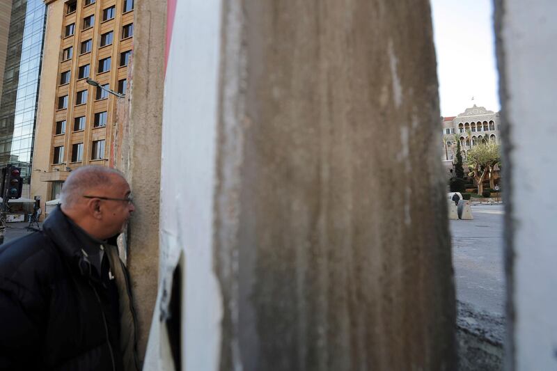 An anti-government protester peers through a gap in a concrete wall installed by authorities to keep protesters far from the main Lebanese government headquarters, far right, and open road to parliament, in downtown Beirut, Lebanon. AP Photo