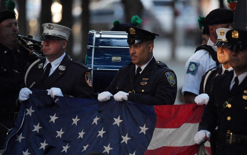 New York police and firefighters hold a US flag as a band plays the US National Anthem at the National 9/11 Memorial during a ceremony commemorating  the 20th anniversary of the 9/11 attacks on the World Trade Center, in New York.  AFP
